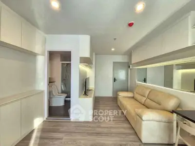Modern living room with sleek design, featuring a cozy beige sofa, wall-mounted TV, and open layout leading to a bathroom.
