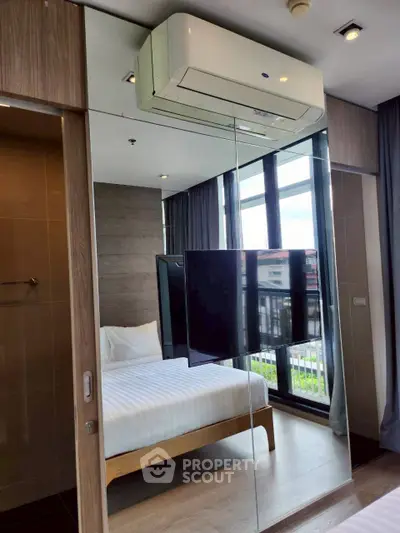 Modern bedroom with mirrored wall and large windows offering natural light.
