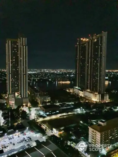 Stunning night view of high-rise buildings with city lights and river backdrop.