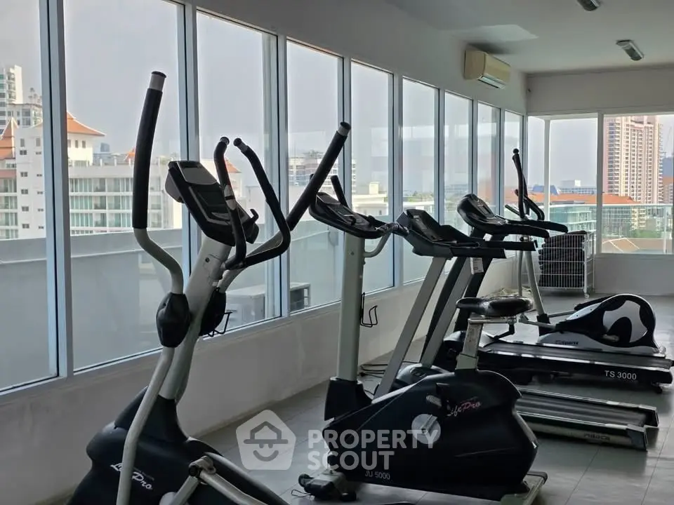 Spacious gym with modern equipment and city view in luxury apartment building.