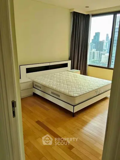 Spacious bedroom with city view and modern furnishings in high-rise apartment.