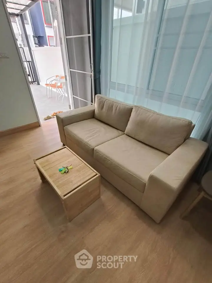 Cozy living room with beige sofa and wooden coffee table, open to a bright outdoor area.