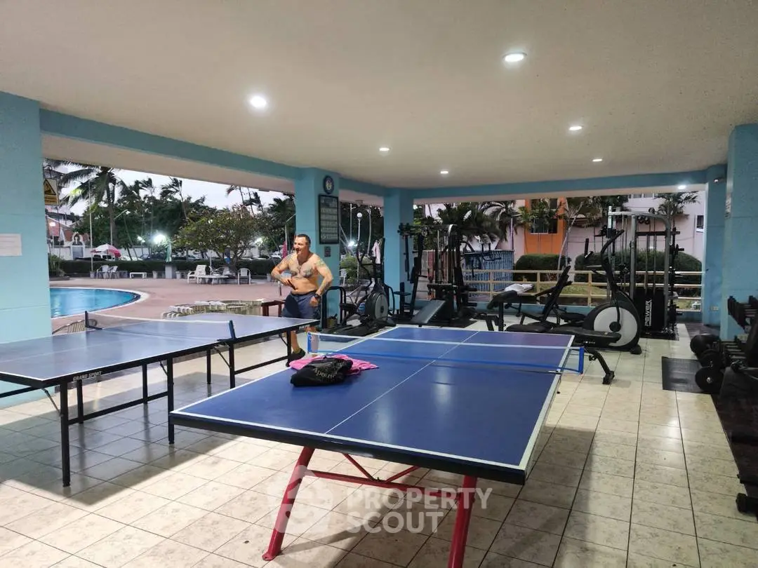 Spacious gym with table tennis and pool view in luxury apartment complex.