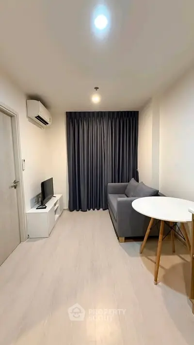 Modern living room with cozy gray sofa, TV, and stylish round table in a minimalist apartment.