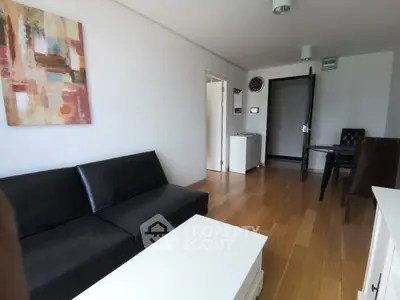 Modern living room with black sofa, wooden floor, and abstract art on white walls.