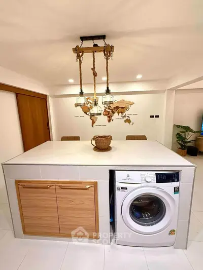 Modern kitchen with island featuring built-in washing machine and stylish lighting.