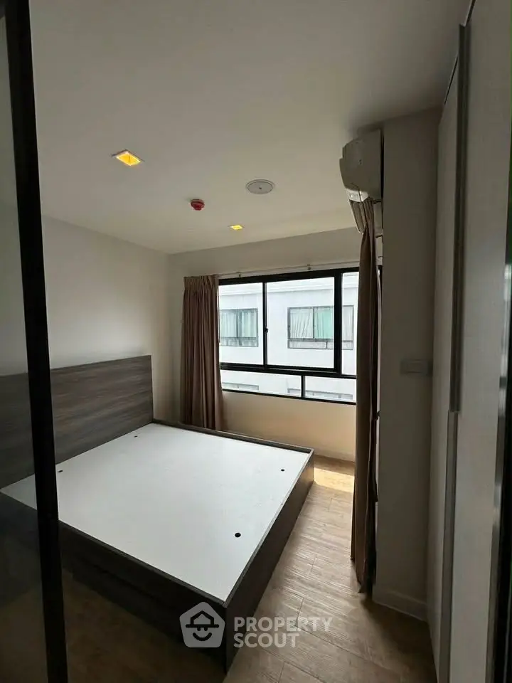Modern bedroom with large window and wooden flooring in a stylish apartment.