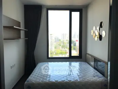 Modern bedroom with large window and city view, featuring a new mattress and stylish wall decor.