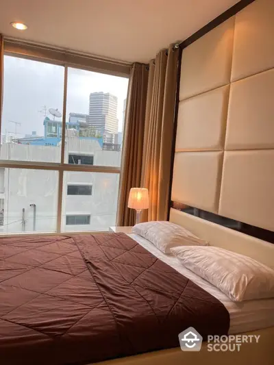 Modern bedroom with large window and city view, featuring elegant decor and cozy ambiance.