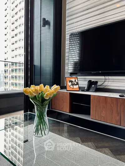 Modern living room with sleek TV setup and glass coffee table, featuring a vase of yellow tulips.
