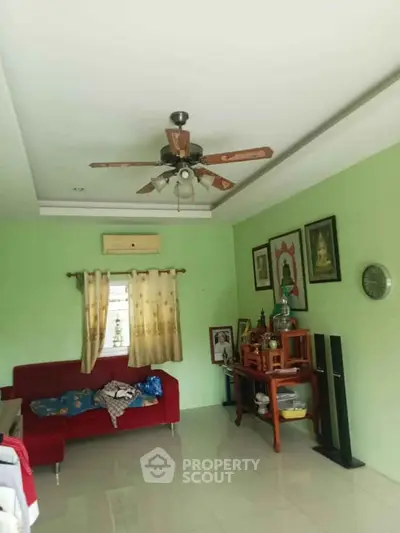 Spacious living room with green walls, ceiling fan, and cozy red sofa.