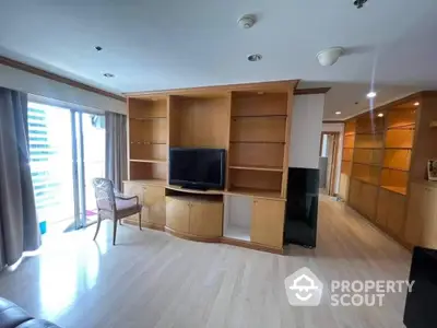 Spacious living room with modern built-in wooden entertainment unit, ample natural light, and sleek flooring, ideal for comfortable urban living.