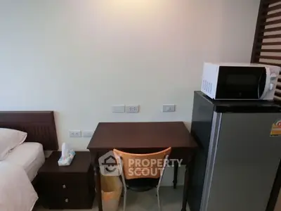 Cozy bedroom with study desk, mini fridge, and microwave in modern apartment.