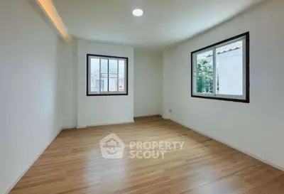 Spacious empty room with wooden flooring and large windows offering natural light.
