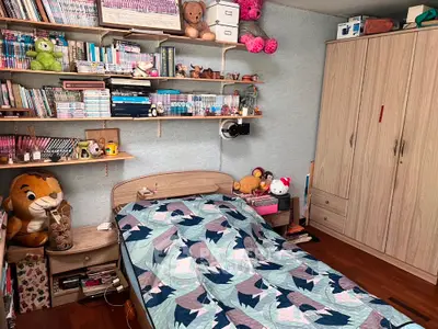 Cozy bedroom filled with personal touches, featuring a comfortable bed, ample shelving with books and toys, and a large wardrobe for storage.