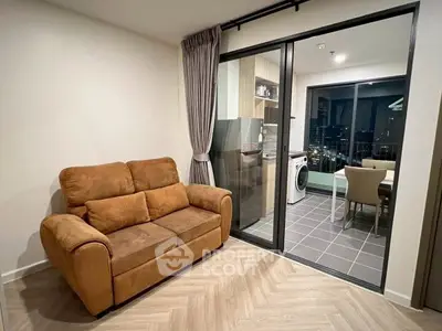 Modern living room with cozy sofa and glass doors leading to a stylish kitchen with city view.