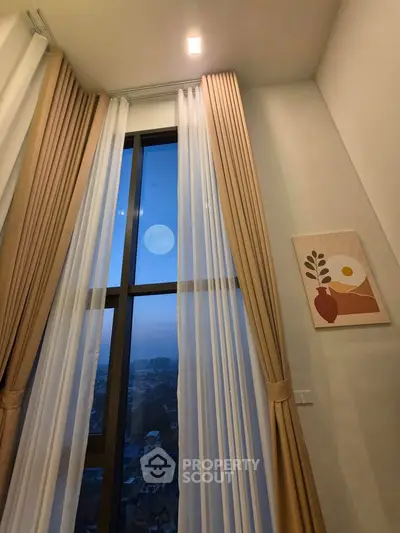 Elegant high-ceiling living room with large window and stylish curtains, offering a stunning city view.