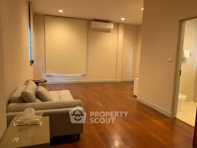 Spacious living room with wooden flooring and modern sofa, featuring air conditioning and natural light.