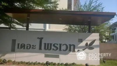 Modern residential building entrance with stylish signage and lush greenery.