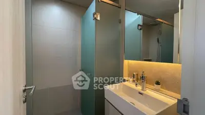 Modern bathroom with sleek design and ambient lighting, featuring a stylish sink and glass shower enclosure.