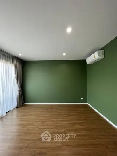Spacious empty room with green accent wall and wooden flooring