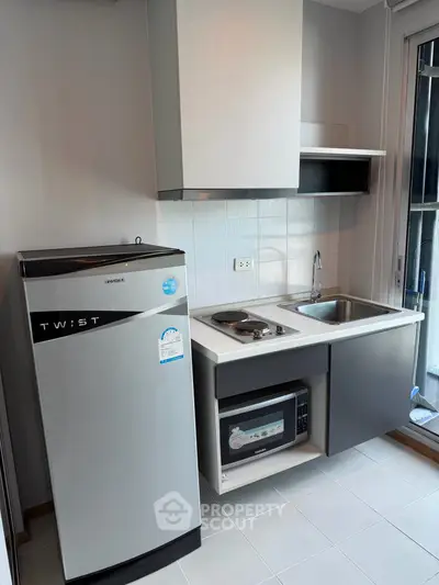 Modern compact kitchen with fridge, stove, and microwave in a sleek apartment.