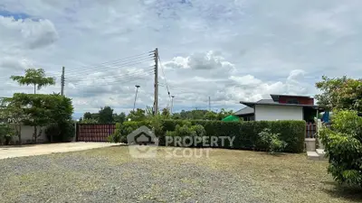 Spacious garden area with modern house and lush greenery under a cloudy sky.