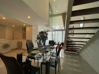 Luxurious modern dining area with glass table, elegant staircase, and open kitchen in a stylish apartment.