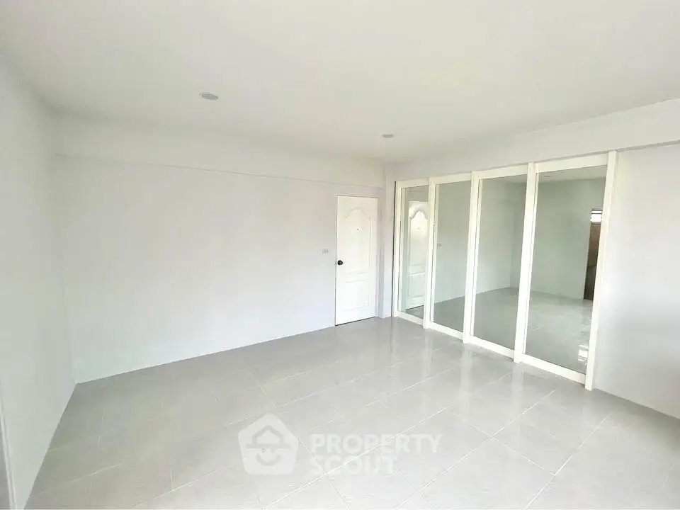 Spacious empty room with white walls and tiled floor, featuring sliding glass doors.
