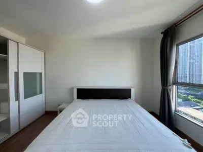 Spacious bedroom with large window offering city views and modern furnishings.