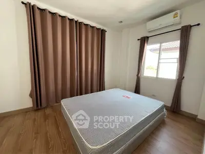 Spacious bedroom with large window and air conditioning, featuring elegant brown curtains and wooden flooring.
