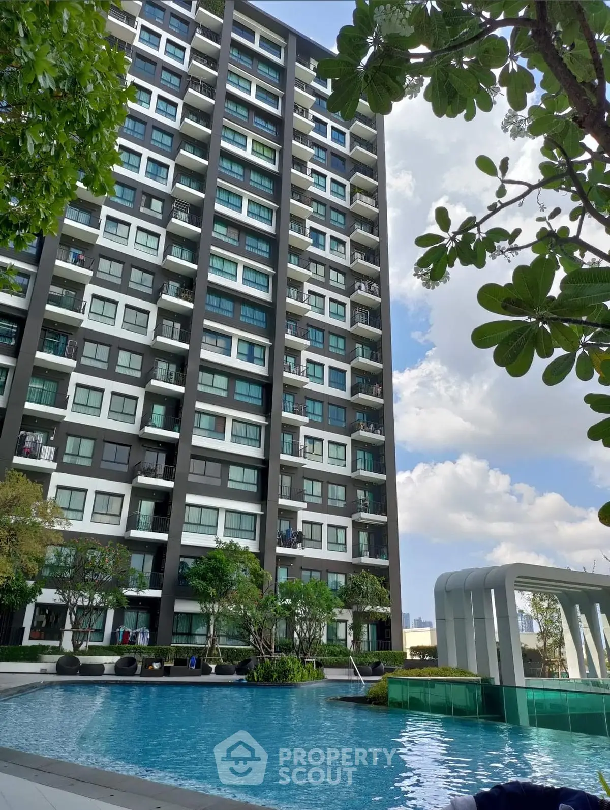 Modern high-rise building with pool and lush greenery under a clear blue sky.