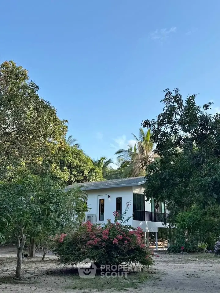 Charming white house surrounded by lush greenery and vibrant flowers, offering serene living in nature.