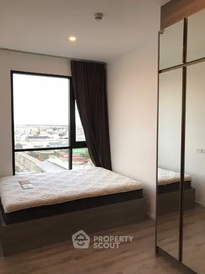 Modern bedroom with large window offering city views, sleek design, and mirrored wardrobe, perfect for urban living.