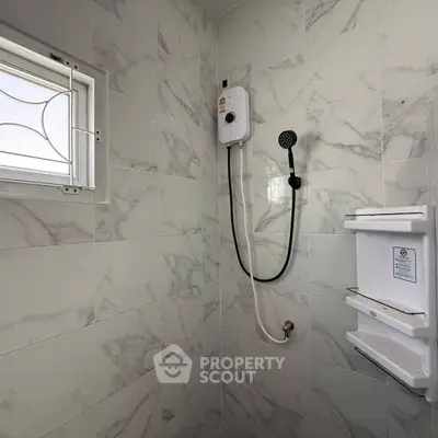 Modern bathroom with marble tiles and electric shower unit, featuring a small window for natural light.