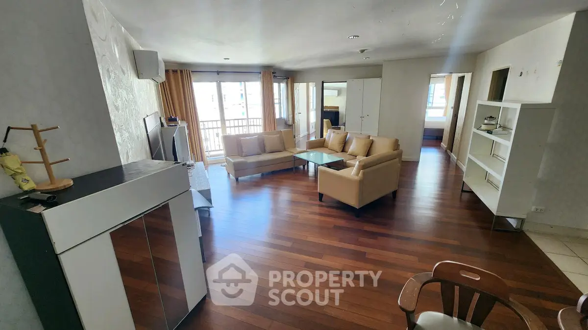 Spacious living room with hardwood floors and modern furniture, featuring large windows for natural light.