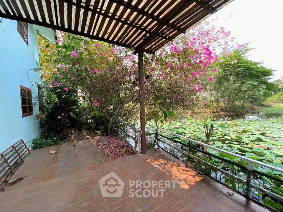Charming outdoor patio with pergola overlooking serene pond and lush greenery, perfect for relaxation.