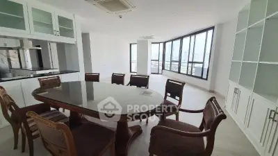 Spacious dining area with elegant table and chairs, large windows offering city views, and modern kitchen setup.
