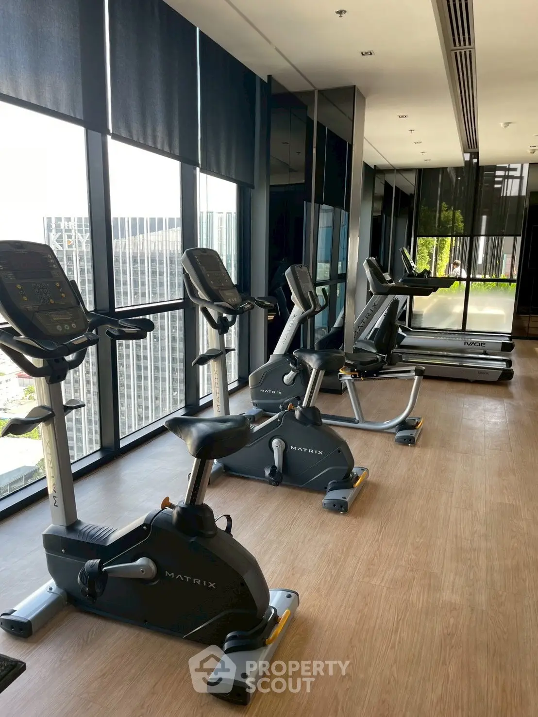 Modern gym with exercise bikes and treadmills in a high-rise building with city views.