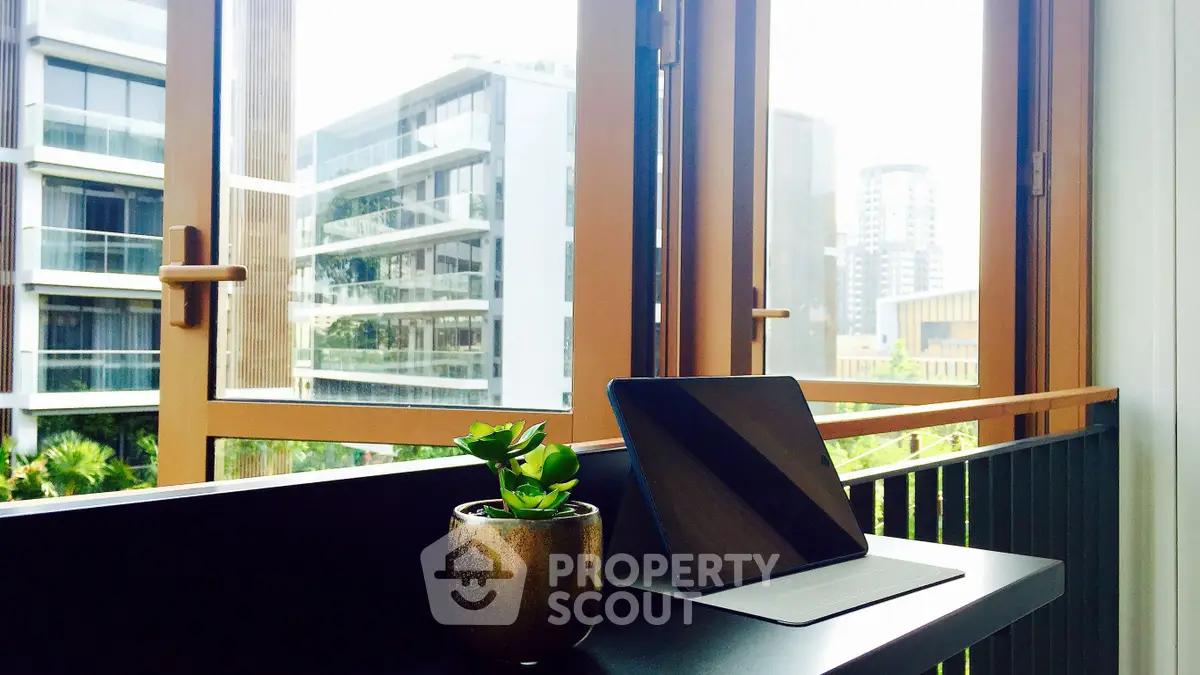 Modern study area with tablet and plant, overlooking urban view through large windows.