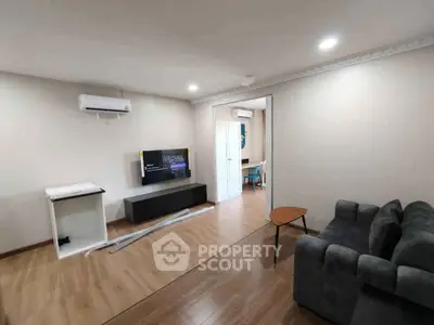 Modern living room with sleek furniture and wooden flooring, featuring a wall-mounted TV and air conditioning.
