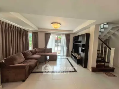 Spacious living room with modern sectional sofa and elegant staircase in a bright, airy home.
