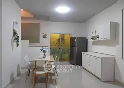 Modern kitchen with dining area, sleek white cabinets, and stainless steel fridge in a cozy apartment.