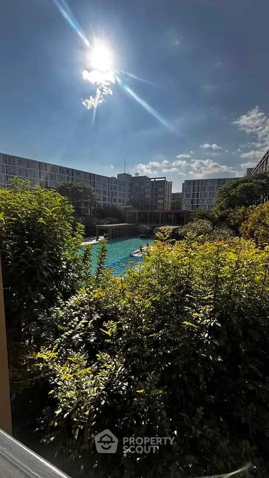 Stunning view of modern apartment complex with lush greenery and sparkling pool under a bright sun.