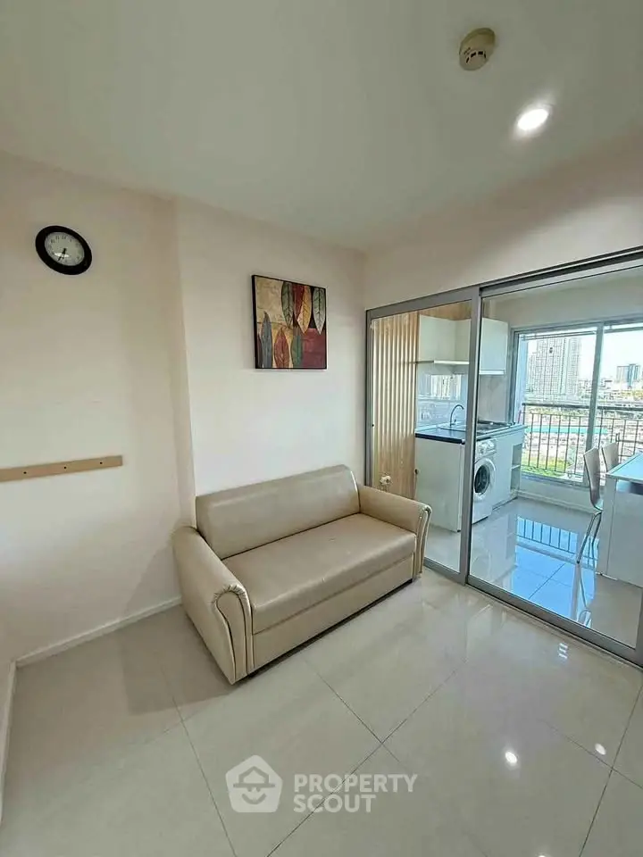 Modern living room with sleek sofa and glass doors leading to a bright kitchen with city view.