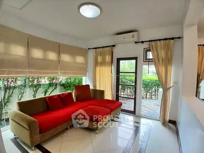 Bright living room with red sofa and garden view, featuring large windows and modern decor.