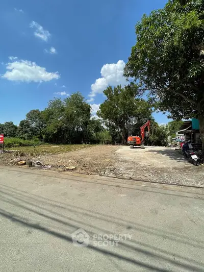 Vacant land plot with trees and construction equipment under clear blue sky.