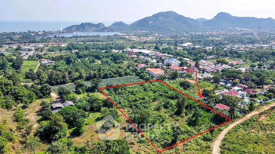 Expansive lush green land parcel available, outlined for clarity, with scenic mountain views and nearby community, ideal for development.