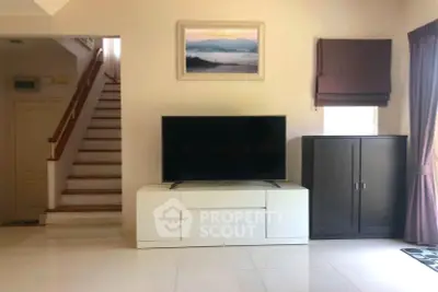 Spacious living room with modern TV setup and elegant staircase in a bright home.