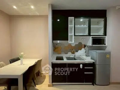 Modern kitchen with sleek black cabinets and dining area, featuring a compact fridge and microwave.
